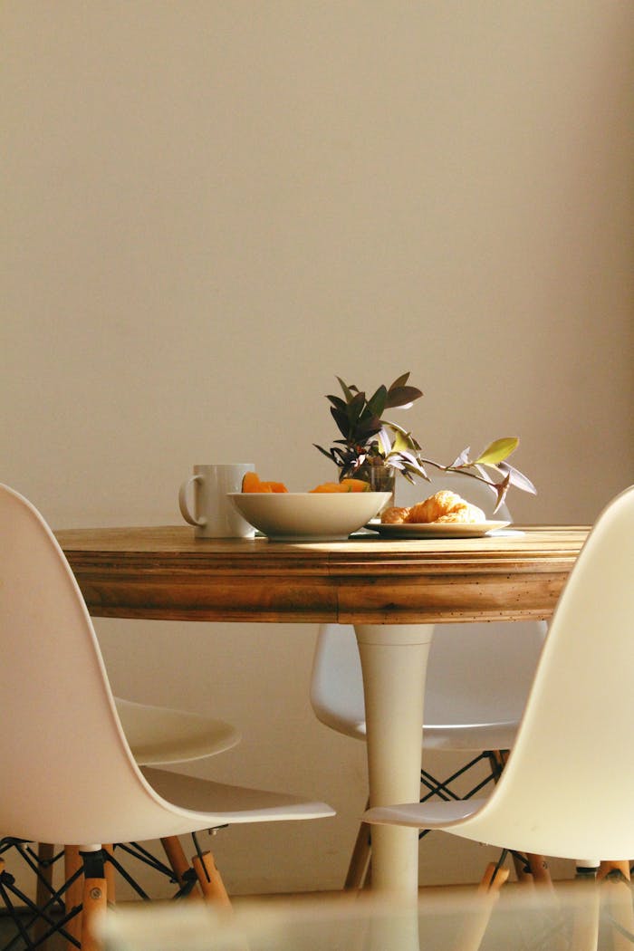 Cozy dining setup with wooden table, chairs, plant, and breakfast items.